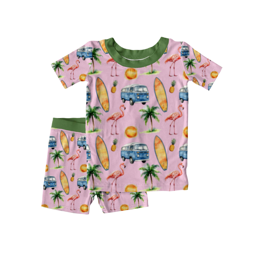 Bamboo kids pajamas with tropical print featuring flamingos, surfboards, palm trees, pineapples, and VW vans on pink with green trim, displayed flat.