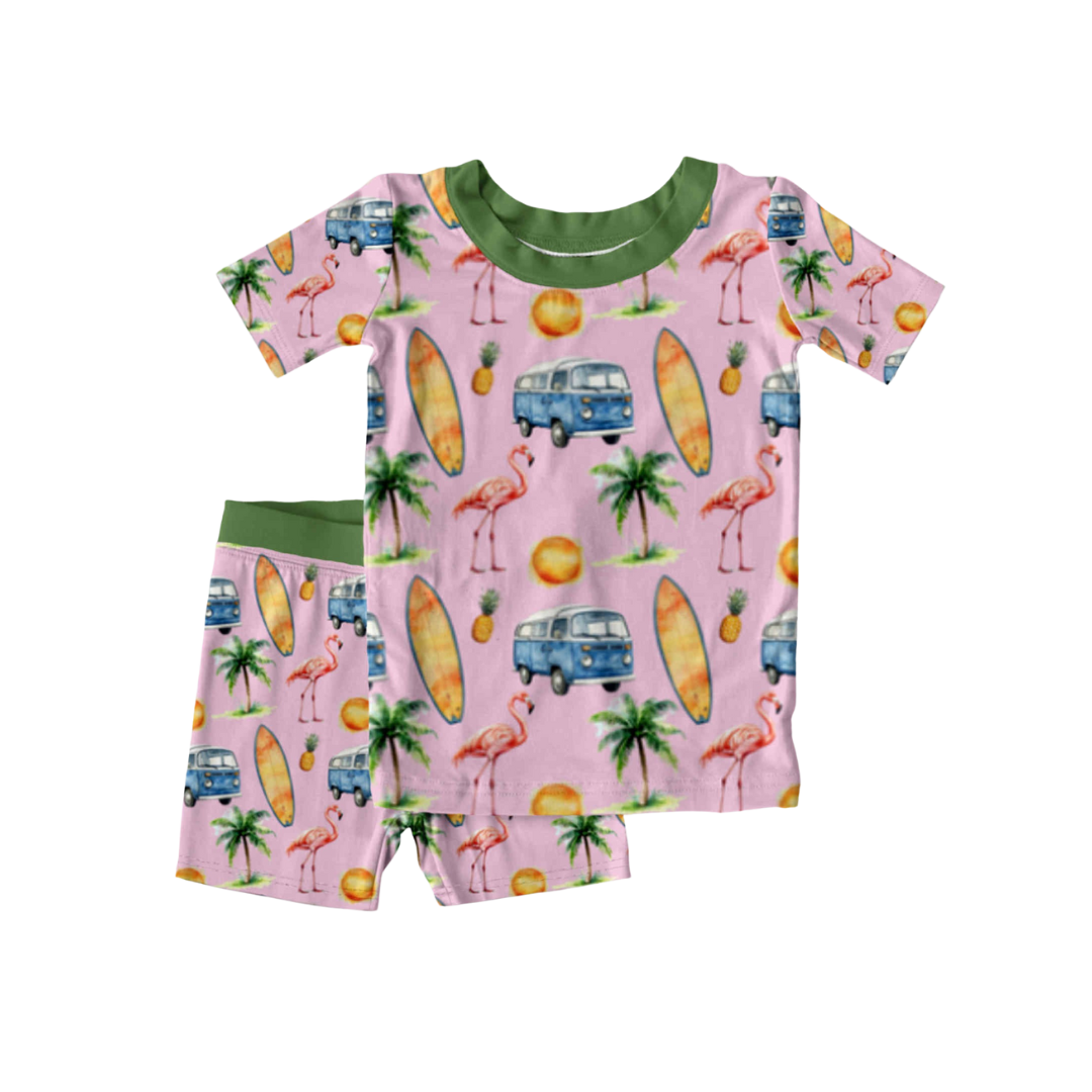 Bamboo kids pajamas with tropical print featuring flamingos, surfboards, palm trees, pineapples, and VW vans on pink with green trim, displayed flat.