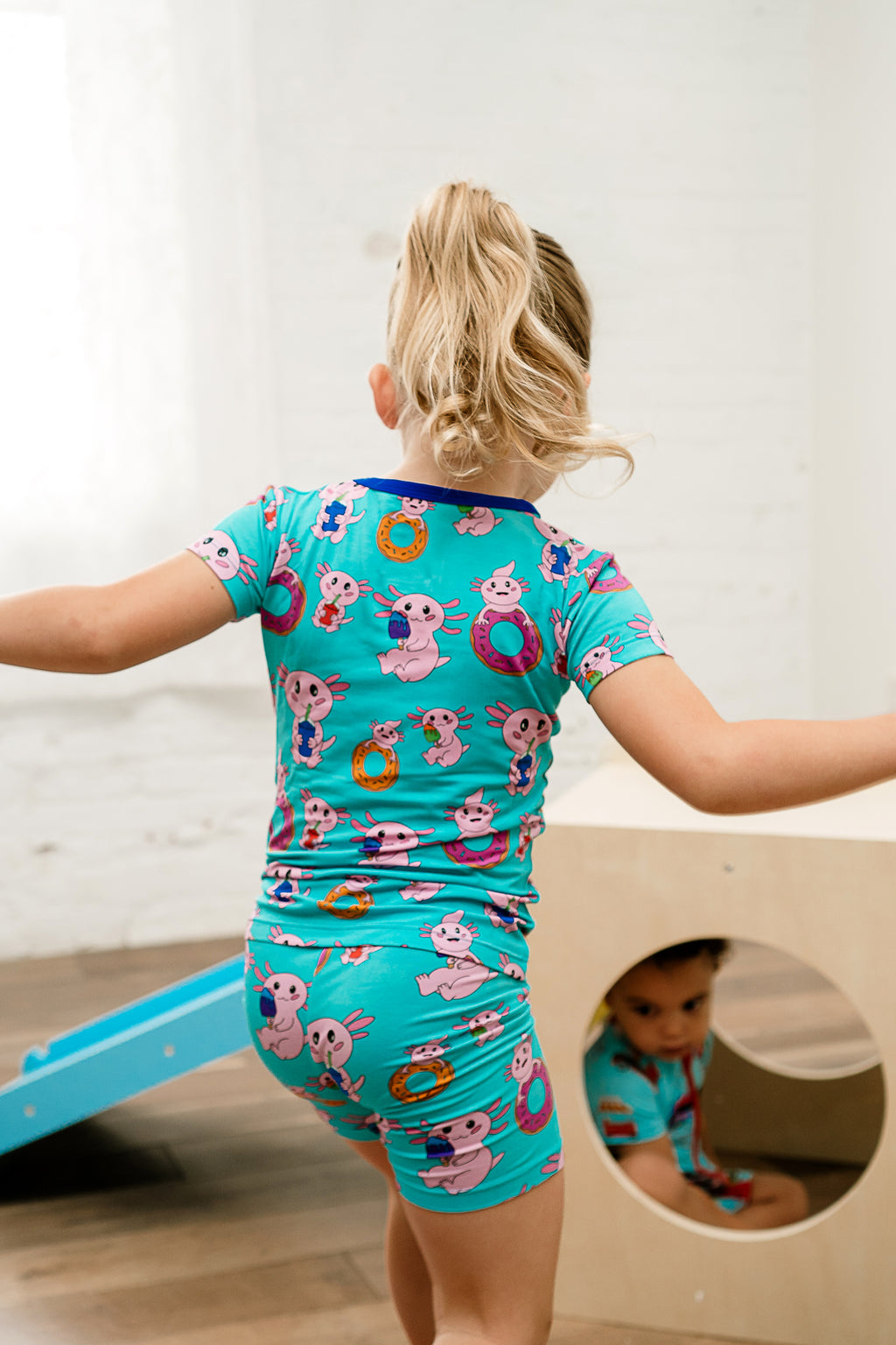 Child twirling joyfully in Axolotlicious bamboo short sleeve and shorts pajamas featuring colorful axolotls.

