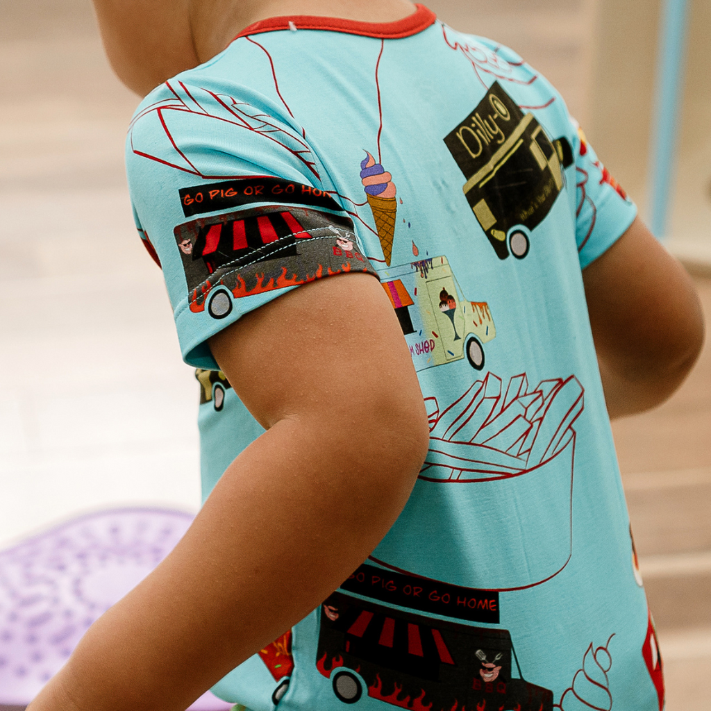 Child wearing a pajama top with a colorful food truck print on the back named Foodie Fun