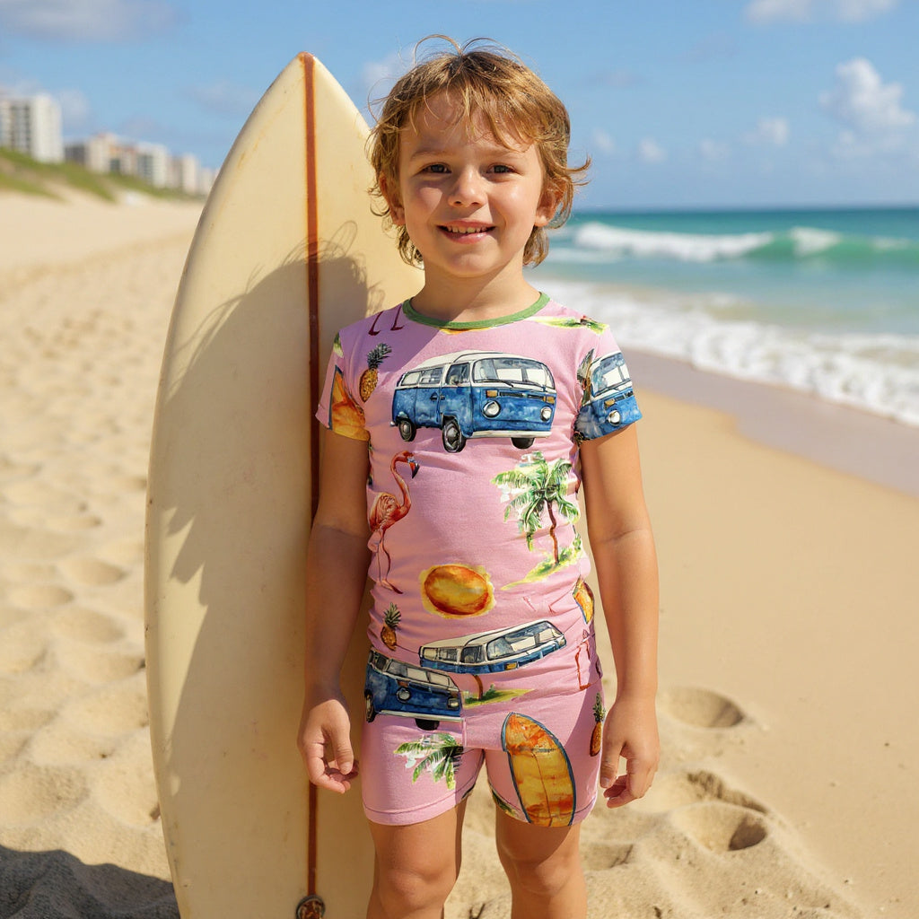 Boy with short wavy hair standing next to a surfboard wearing surf themed pajamas