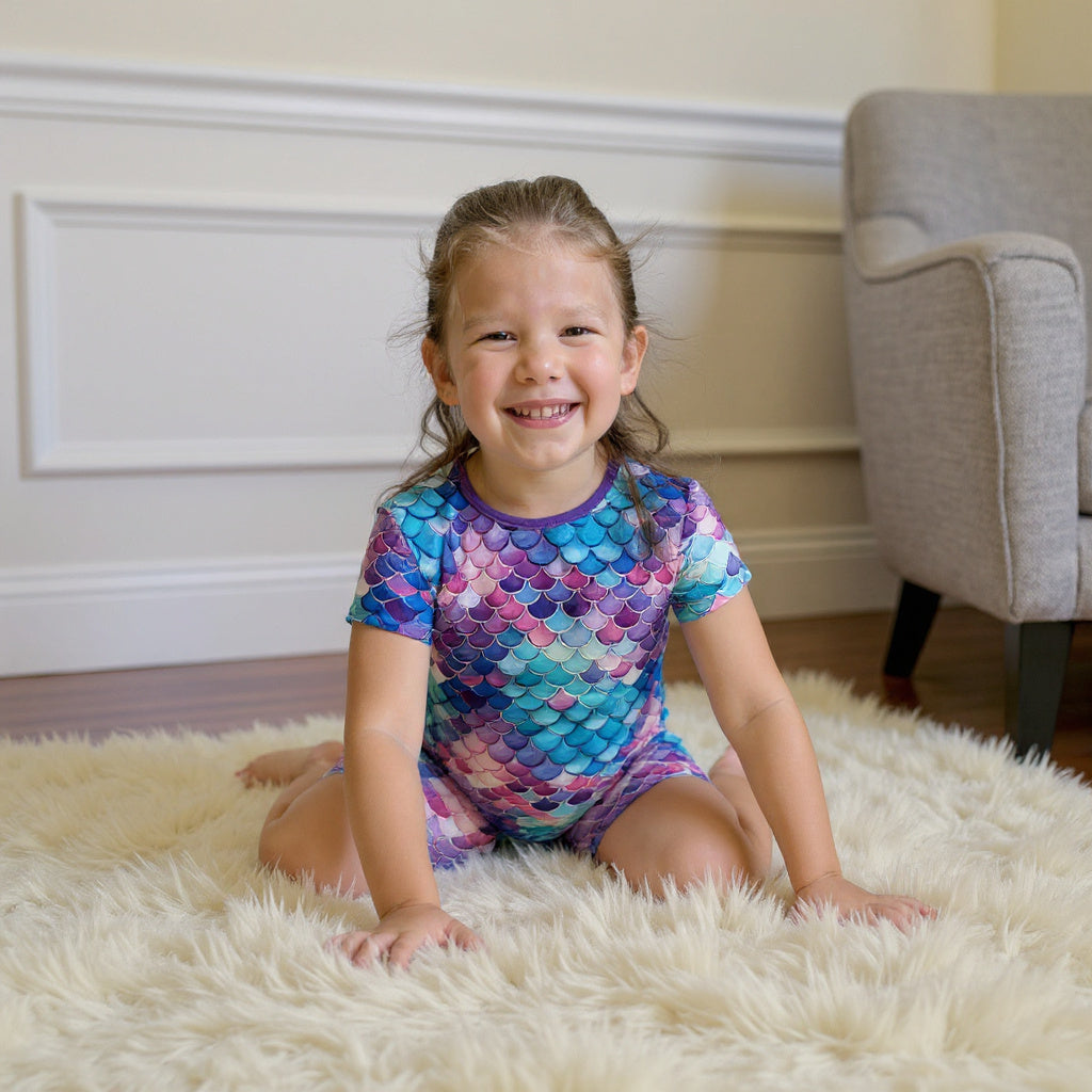 young girl wearing mermaid pajamas sitting on a rug