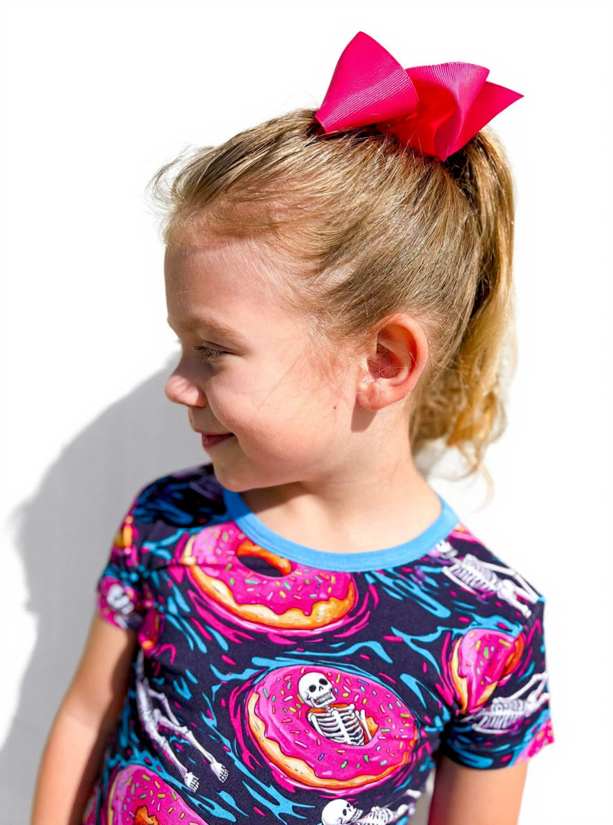 A young girl wearing skeleton and donut pajamas standing in front of a white wall.